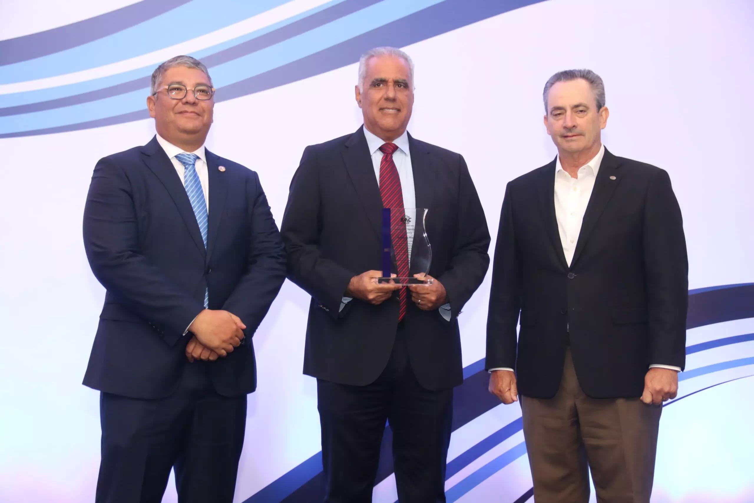 En el centro, el presidente saliente BASC Dominicana, Armando Rivas, recibe un reconocimiento del presidente entrante, Horacio Loma, y del vicepresidente ejecutivo de la Cámara Americana de Comercio, William Malamud. Se resaltó que las certificaciones de comercio seguro favorecen a empresas dominicanas.